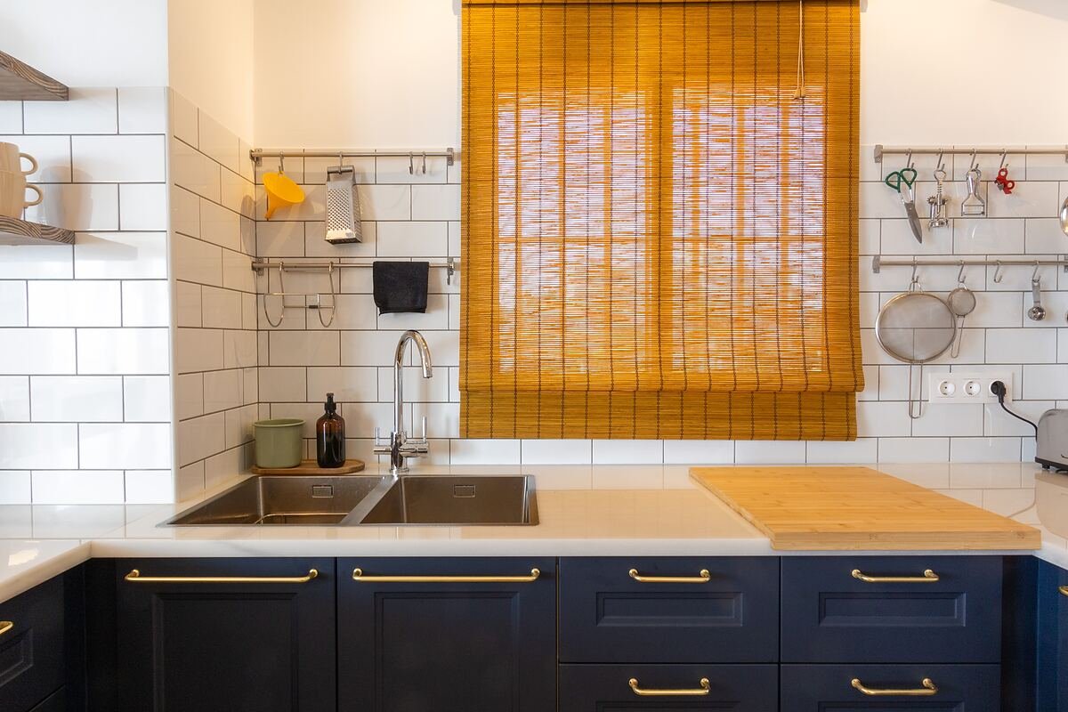 Casa en Gran Alacant: cocina con frente de azulejo blanco, muebles azul marino y estor de bambú sobre el fregadero