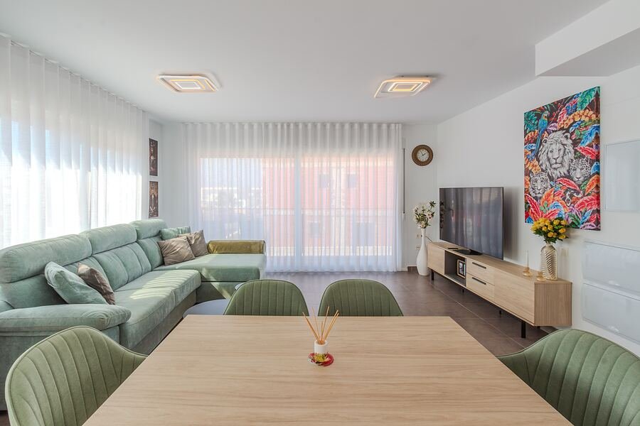 Dúplex Gran Alacant: salón con sofá verde menta, mesa de comedor de madera y un cuadro de colores